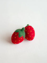 Two red strawberry-shaped objects with green leaves on a light gray background