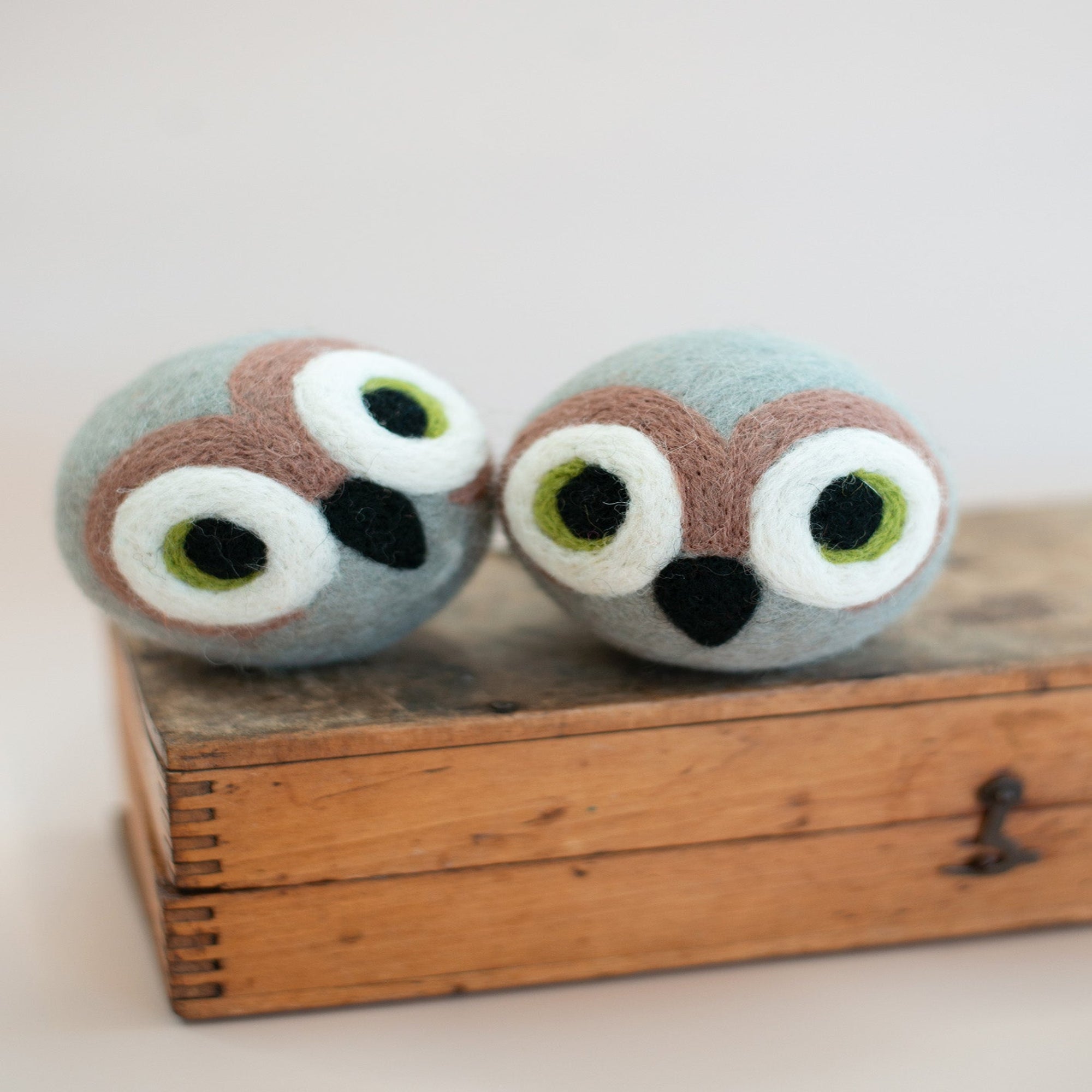 Two owl-shaped bath bombs on a wooden box with a light background
