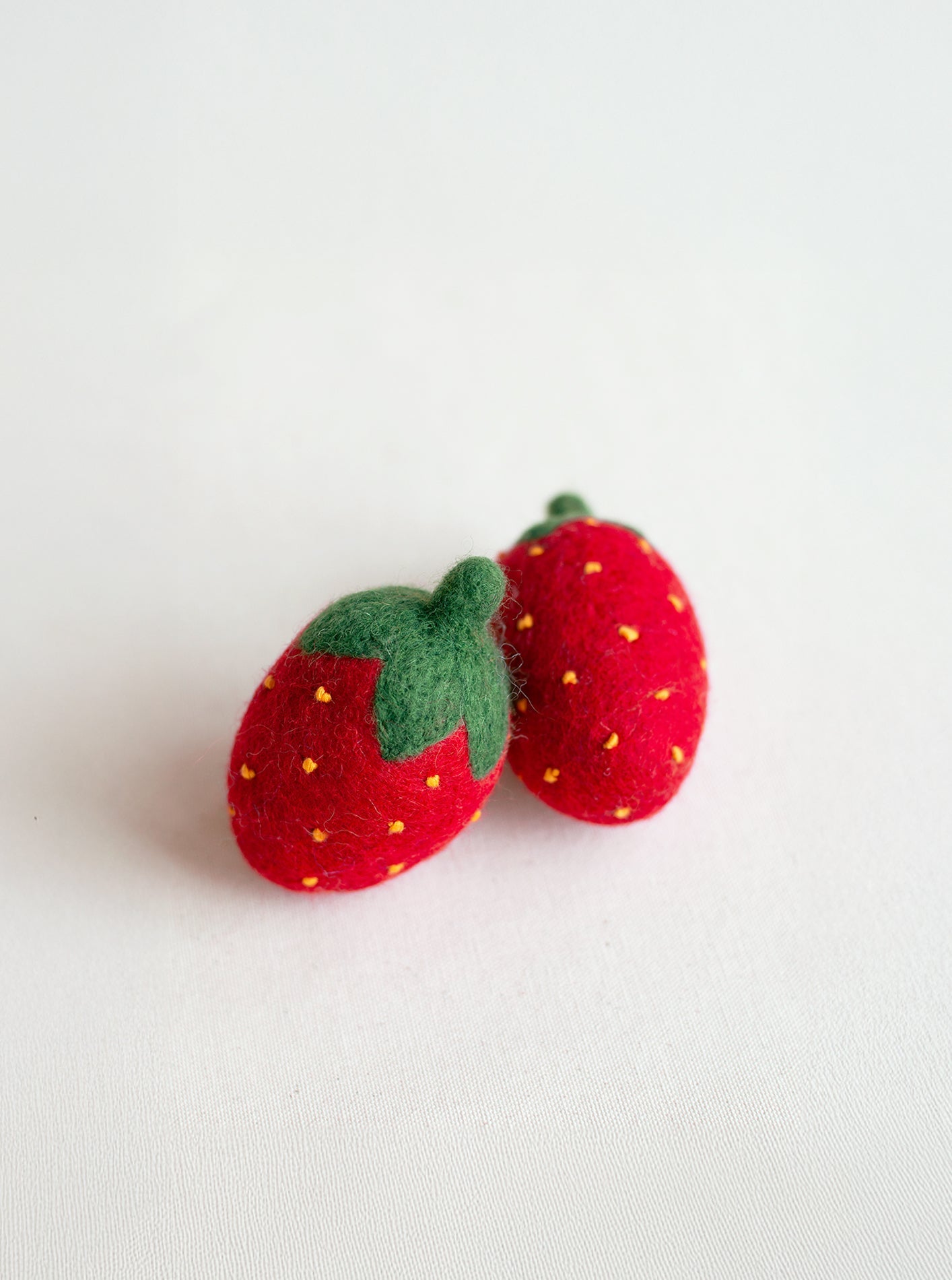 Two red strawberry-shaped objects with green leaves on a light gray background