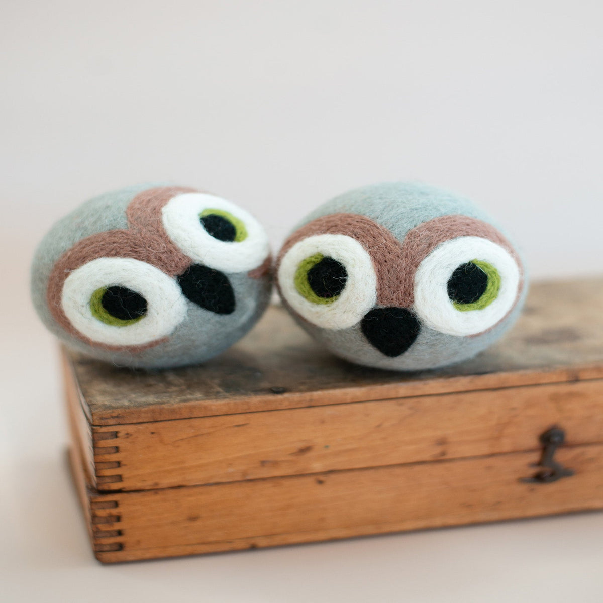 Two owl-shaped bath bombs on a wooden box with a light background